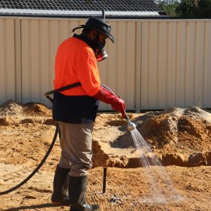Pest control technician hand-spraying liquid termiticide directly onto soil which will have a concrete ground slab poured on top. This pre-construction termite management system is primary only used in Western Australia, where hand-sprayed termite treatments are still allowed to protect buildings.